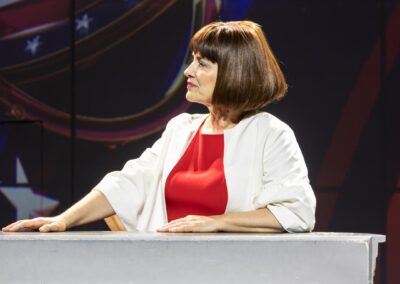 Une comédienne accoudée à un pupitre jouant une politicienne